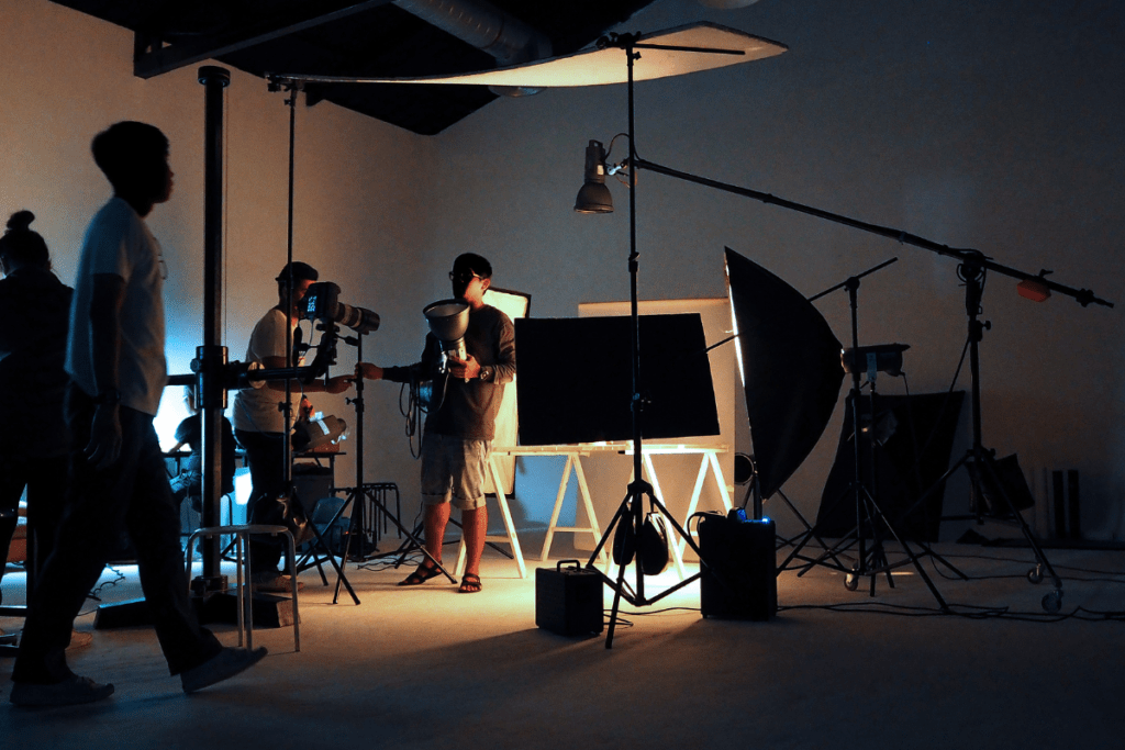 Professional photography studio setup with crew working on set, featuring softboxes, lighting equipment, and camera operators in dimly lit environment