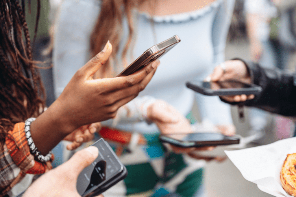 Social media users looking at smartphones together, showing diverse hands holding mobile devices in casual group setting